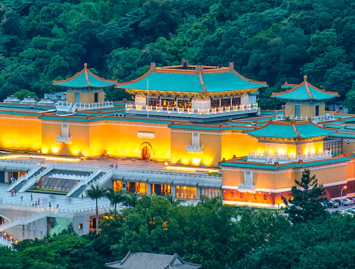 National Palace Museum illuminated at night, surrounded by lush greenery in Taipei, Taiwan.