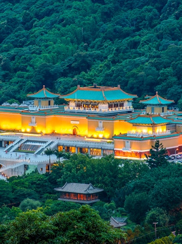 National Palace Museum illuminated at night, surrounded by lush greenery in Taipei, Taiwan.