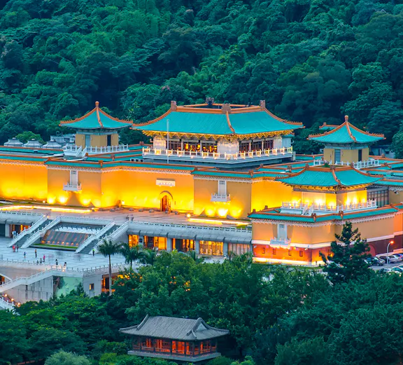 National Palace Museum illuminated at night, surrounded by lush greenery in Taipei, Taiwan.