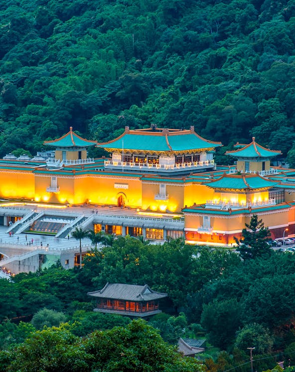 National Palace Museum illuminated at night, surrounded by lush greenery in Taipei, Taiwan.