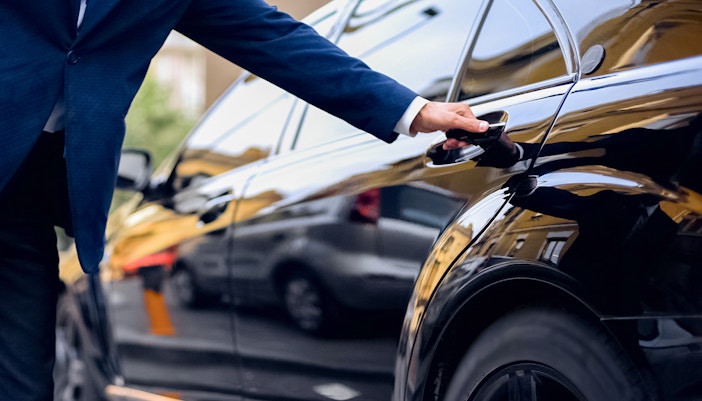 Driver opening backseat door of a black car for transfer service.