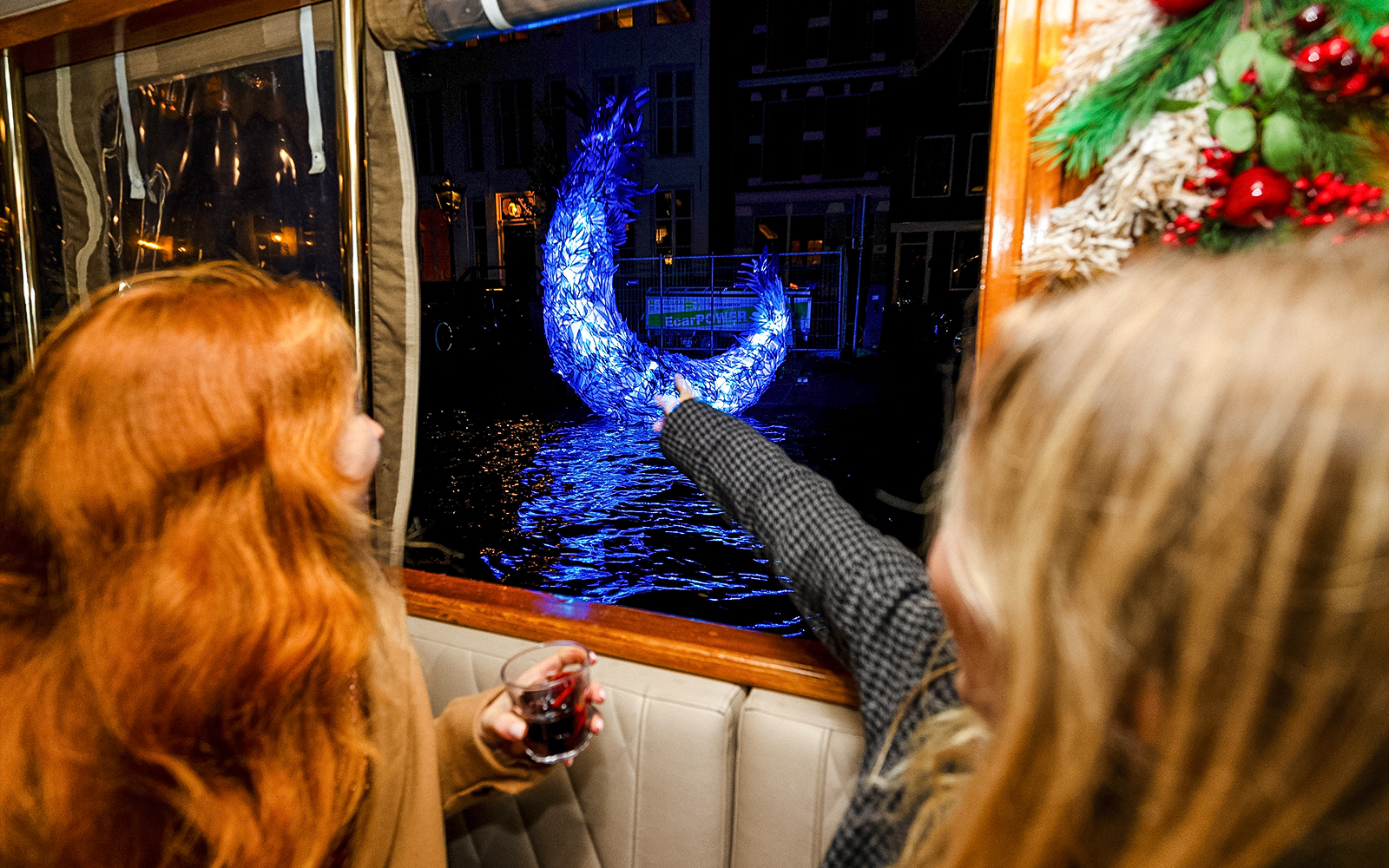 Passengers view illuminated sculpture from boat during Amsterdam Light Festival cruise.