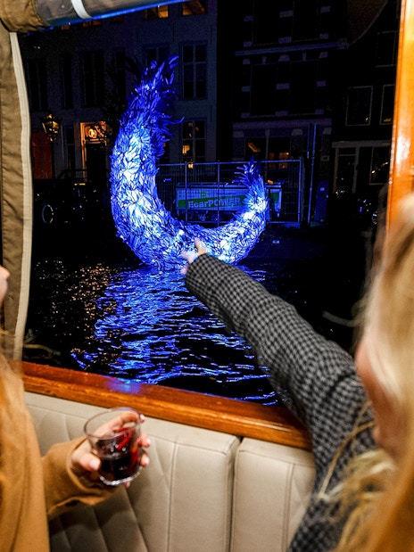 Passengers view illuminated sculpture from boat during Amsterdam Light Festival cruise.
