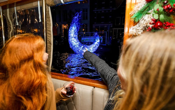 Passengers view illuminated sculpture from boat during Amsterdam Light Festival cruise.
