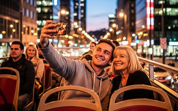 Tourists taking a selfie on a hop-on hop-off bus in a city at night.