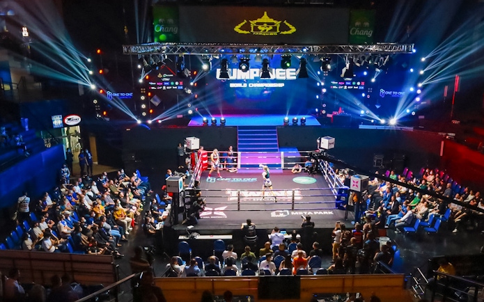 Muay Thai match at One Lumpinee Stadium with audience and stage lights.