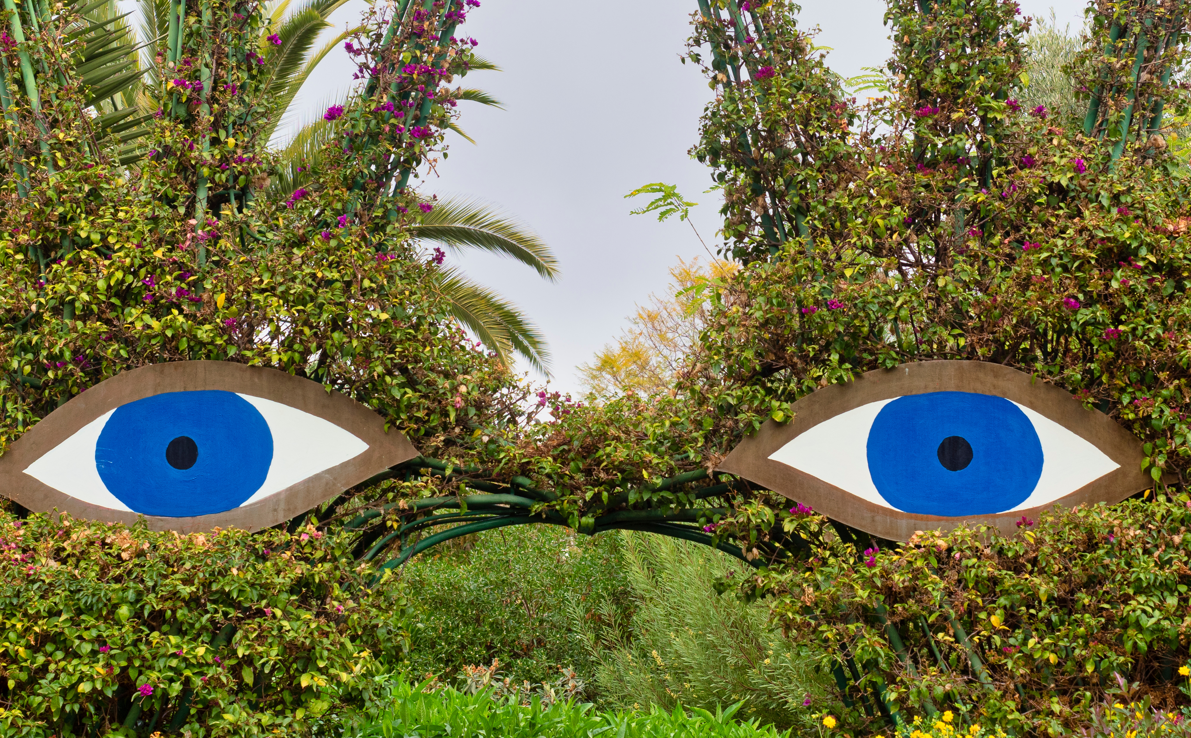 Sculpture of large blue eyes surrounded by greenery at ANIMA Garden.