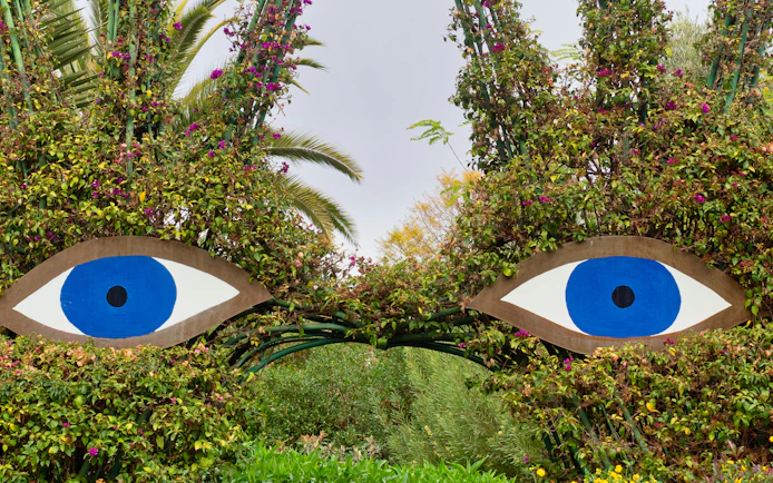 Sculpture of large blue eyes surrounded by greenery at ANIMA Garden.