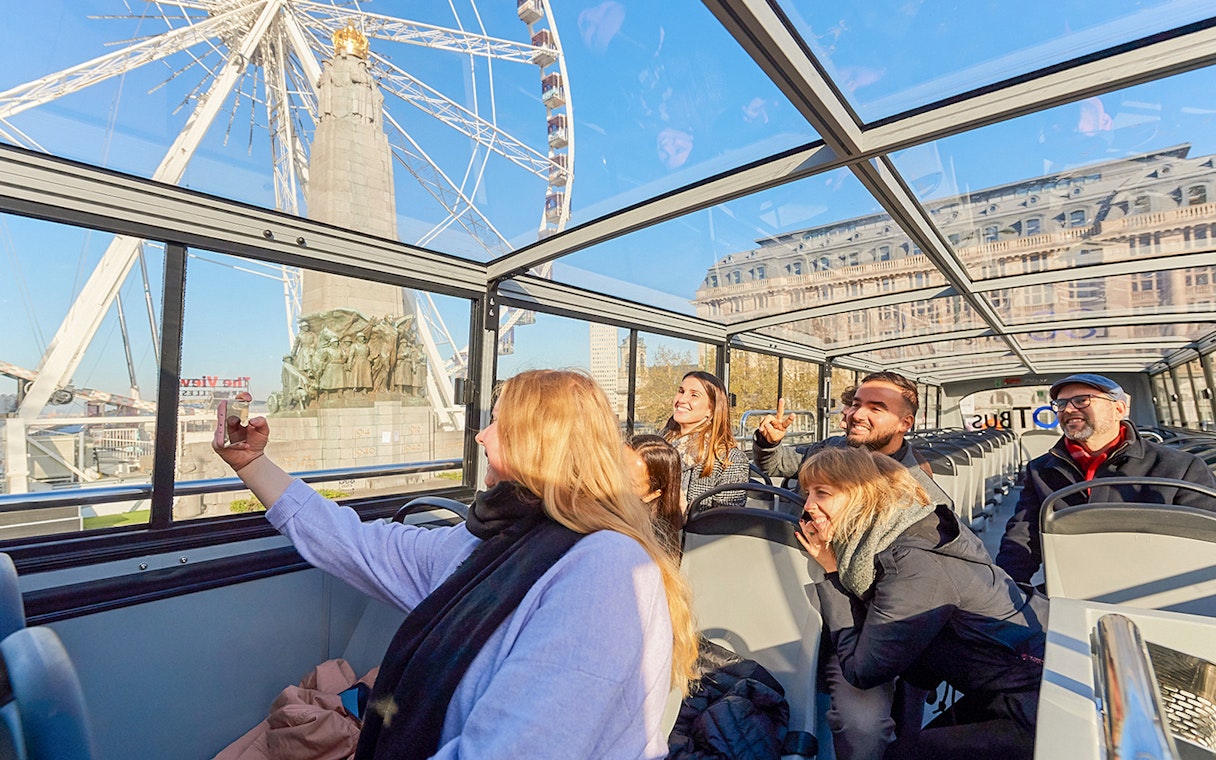 Tourists enjoying Brussels Discovery Hop on Hop off bus tour with Ferris wheel view.
