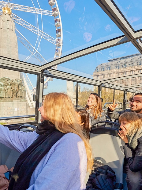 Tourists enjoying Brussels Discovery Hop on Hop off bus tour with Ferris wheel view.