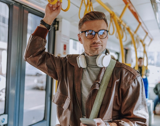 Man holding onto tram handrail with headphones around neck.
