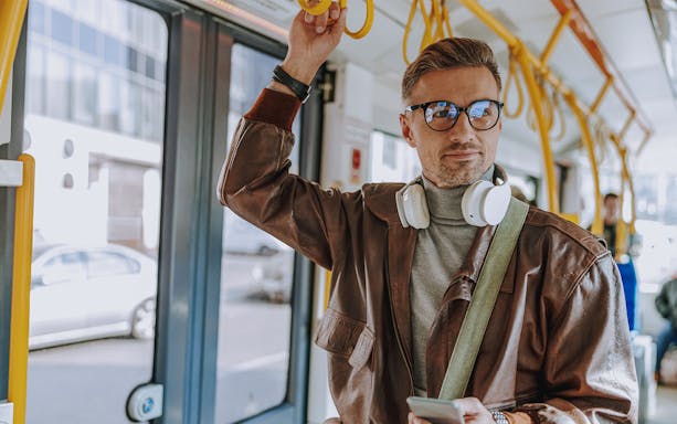 Man holding onto tram handrail with headphones around neck.