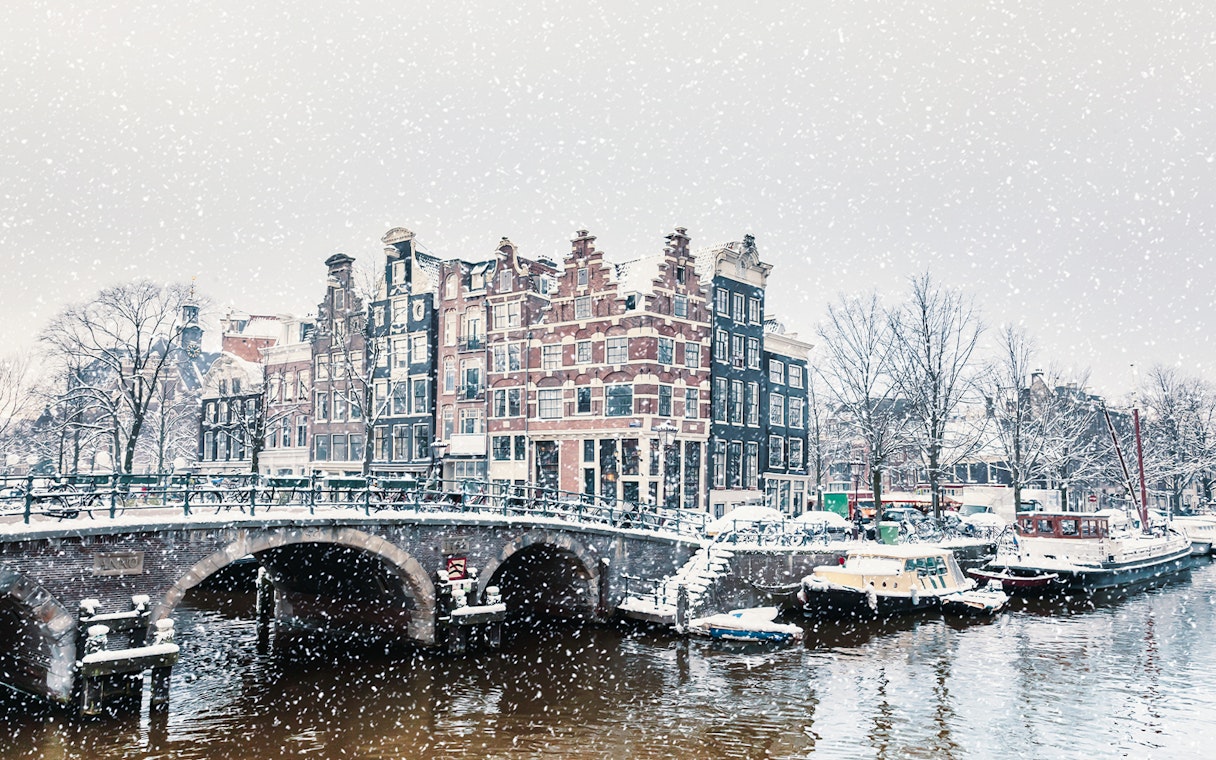Winter snowfall over a canal with traditional Dutch houses in Amsterdam.