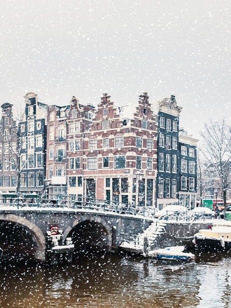 Winter snowfall over a canal with traditional Dutch houses in Amsterdam.