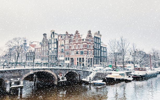 Winter snowfall over a canal with traditional Dutch houses in Amsterdam.