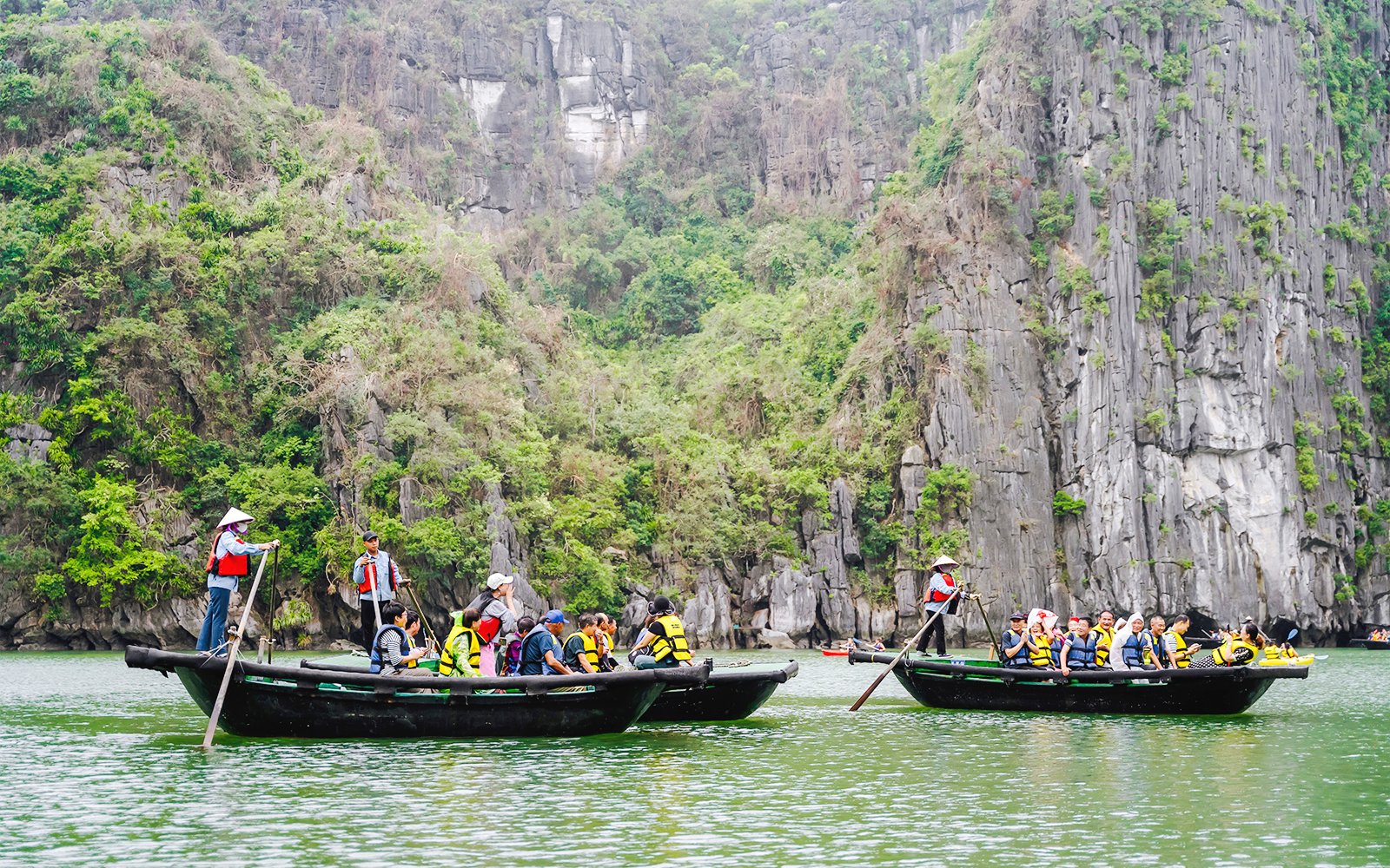 Bamboo boats with tourists on a ride to Sung Sot Cave, surrounded by limestone cliffs in Vietnam.