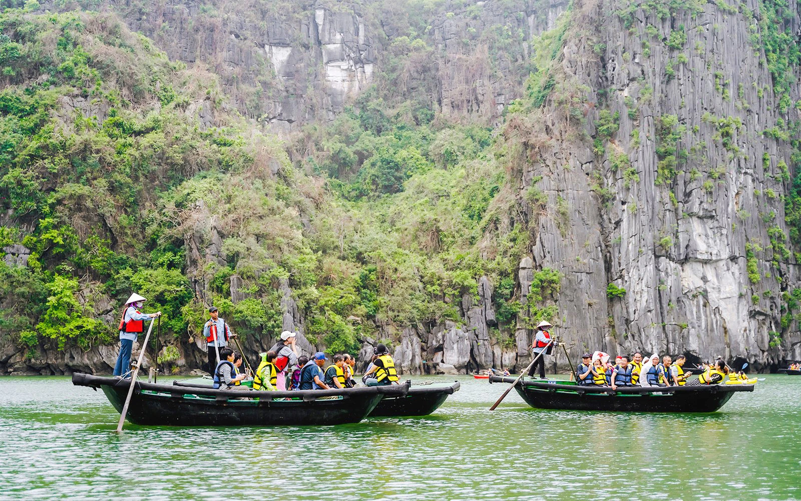 Bamboo boats with tourists on a ride to Sung Sot Cave, surrounded by limestone cliffs in Vietnam.