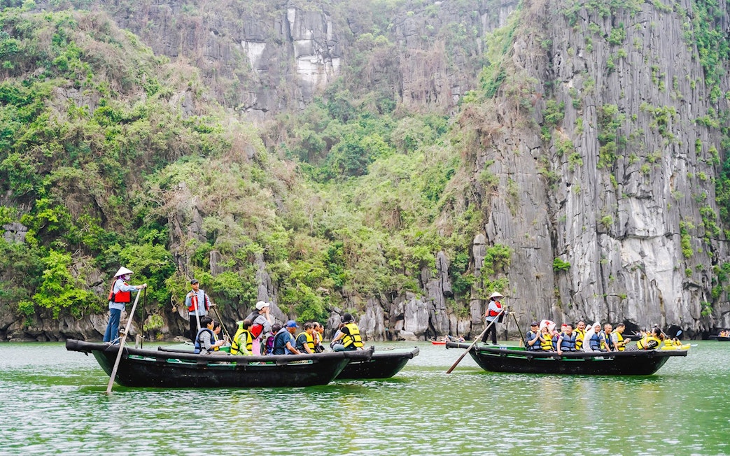 Bamboo boats with tourists on a ride to Sung Sot Cave, surrounded by limestone cliffs in Vietnam.