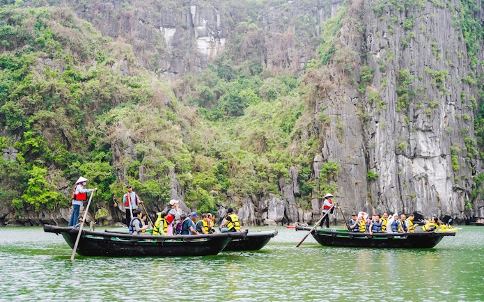 Bamboo boats with tourists on a ride to Sung Sot Cave, surrounded by limestone cliffs in Vietnam.