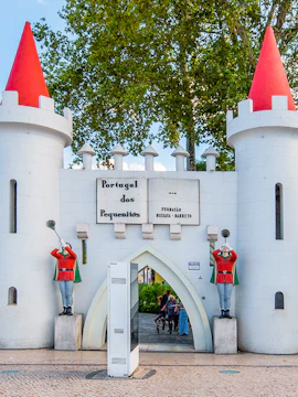 Entrance gate of Portugal dos Pequenitos with two guard statues and red-roofed towers.