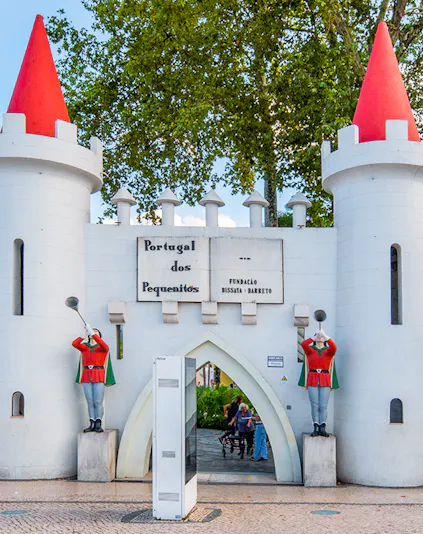 Entrance gate of Portugal dos Pequenitos with two guard statues and red-roofed towers.