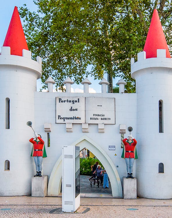 Entrance gate of Portugal dos Pequenitos with two guard statues and red-roofed towers.
