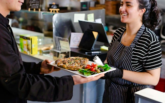 Server presenting a dish with salad and olives during a food tour at Pike Place Market.
