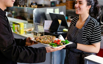 Server presenting a dish with salad and olives during a food tour at Pike Place Market.