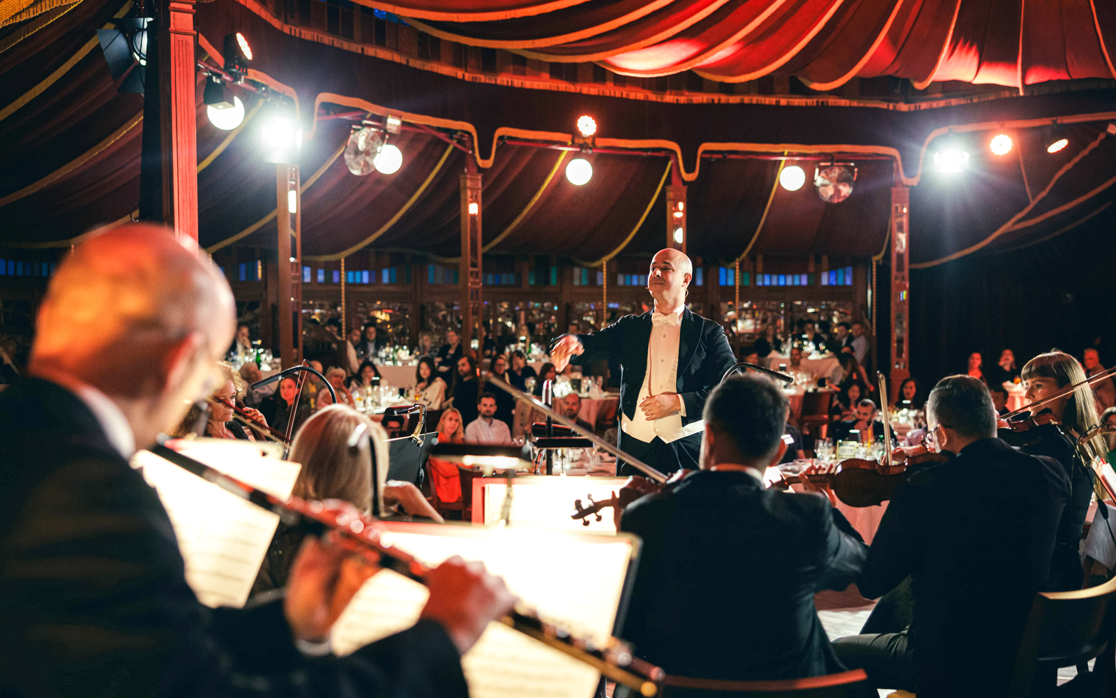 Conductor leading orchestra at Strauss concert in Prater Vienna with audience dining.