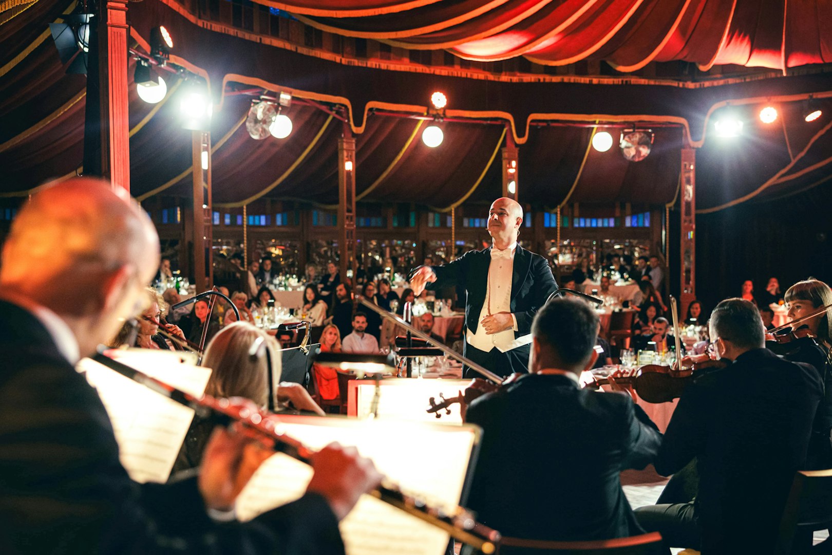 Conductor leading orchestra at Strauss concert in Prater Vienna with audience dining.