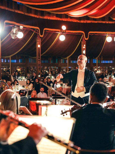 Conductor leading orchestra at Strauss concert in Prater Vienna with audience dining.