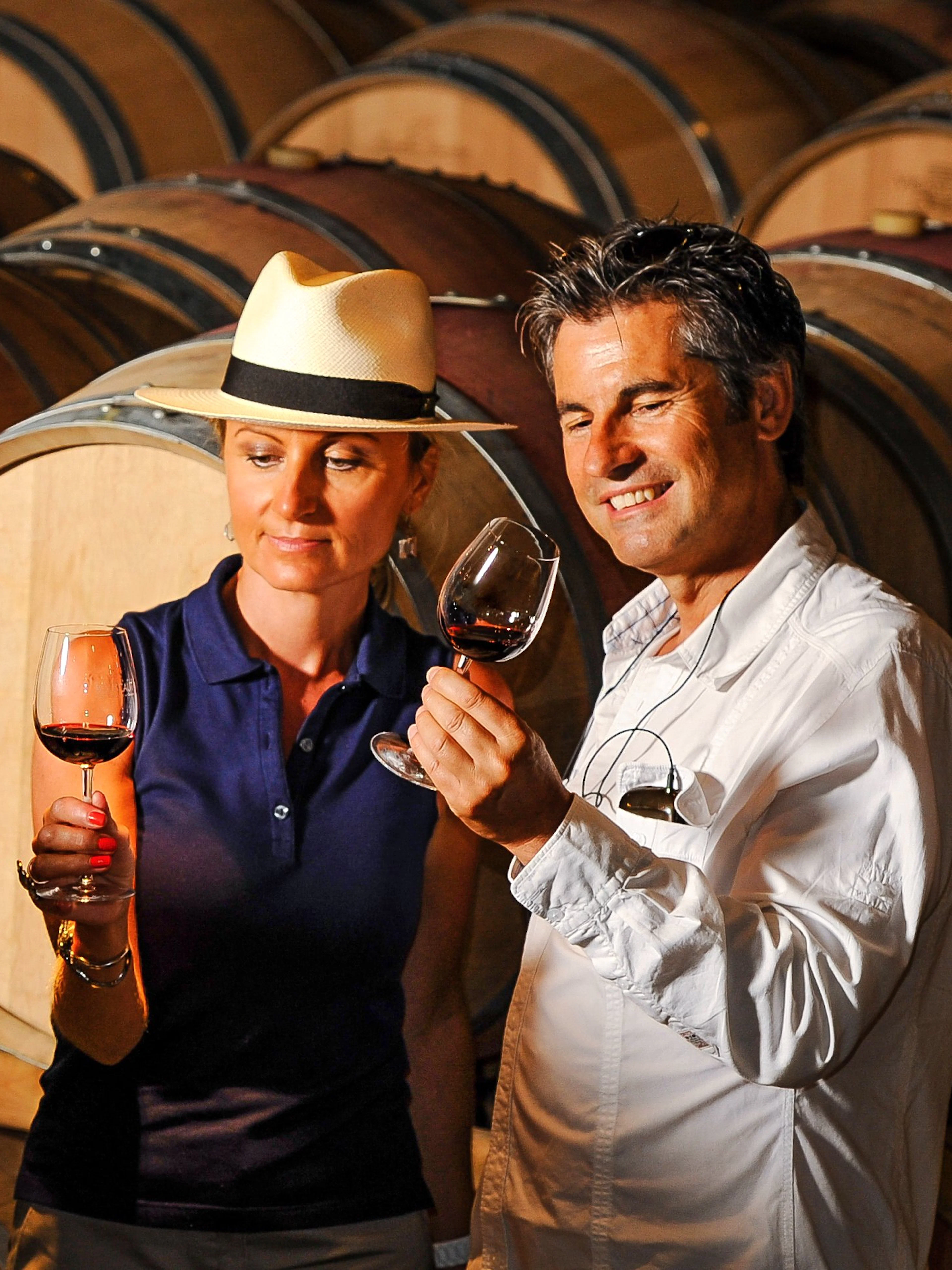 Couple tasting wine in a cellar with wooden barrels in the background.
