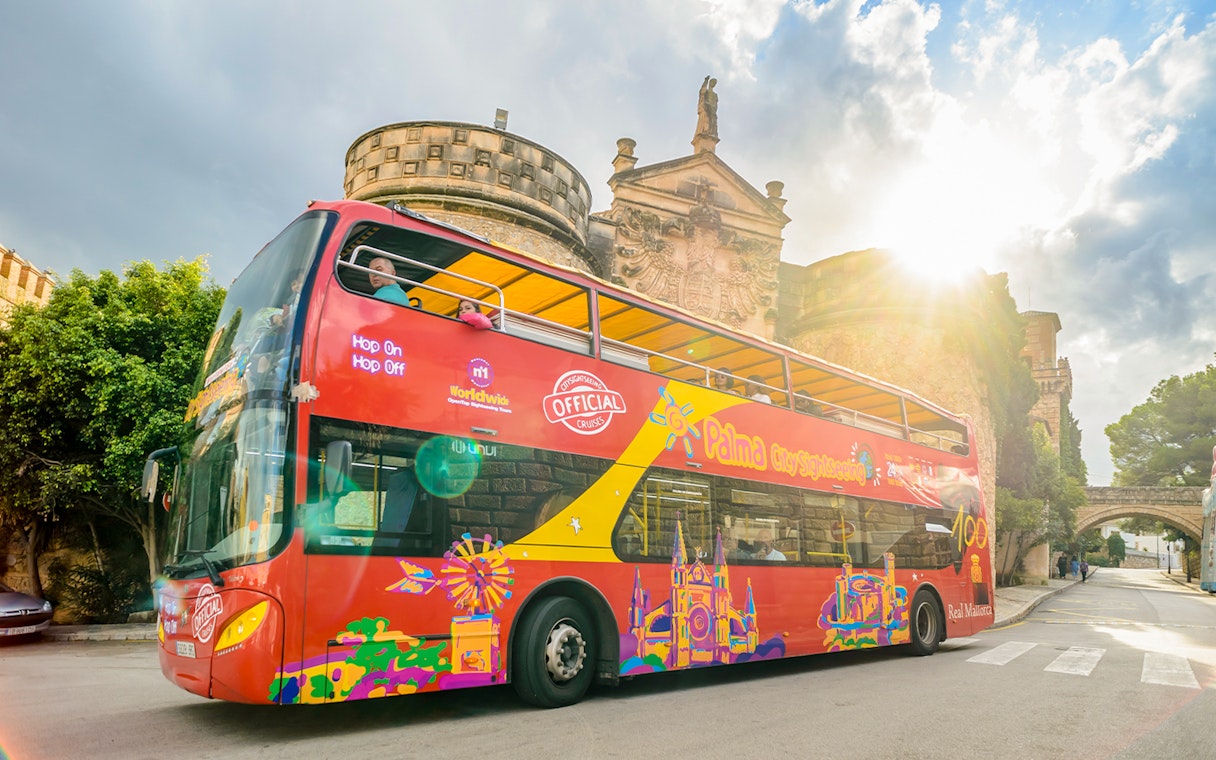 Red double-decker bus on Palma de Mallorca hop-on hop-off tour near historic building.