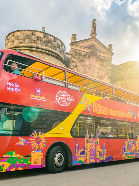 Red double-decker bus on Palma de Mallorca hop-on hop-off tour near historic building.