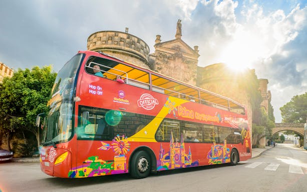 Red double-decker bus on Palma de Mallorca hop-on hop-off tour near historic building.