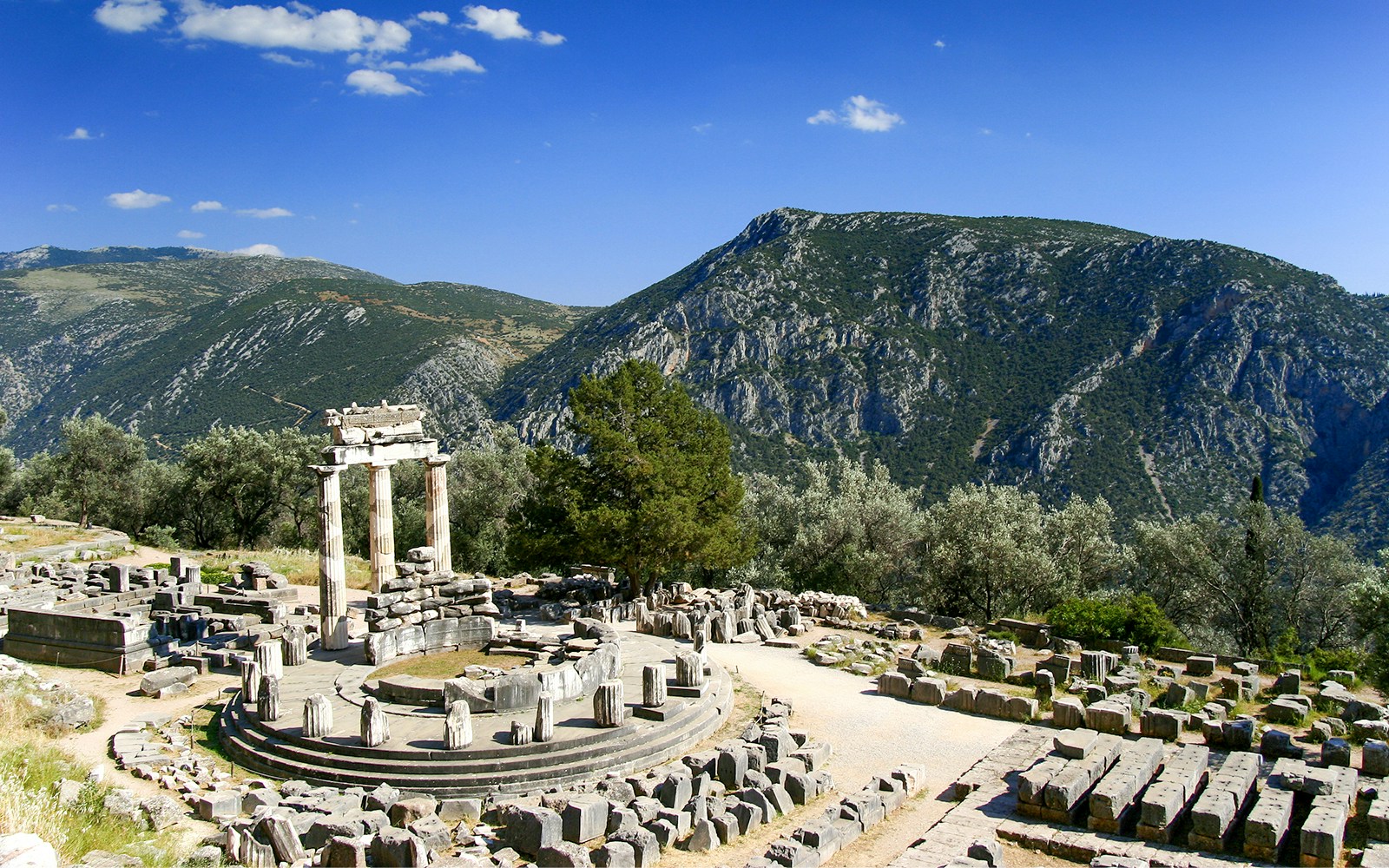 Ancient ruins of the Tholos at Delphi archaeological site, Greece, with mountains in the background.