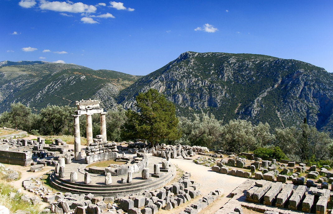 Ancient ruins of the Tholos at Delphi archaeological site, Greece, with mountains in the background.