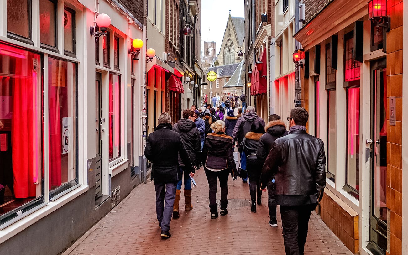 Tour group exploring Amsterdam Red Light District at night with illuminated buildings and bustling streets.
