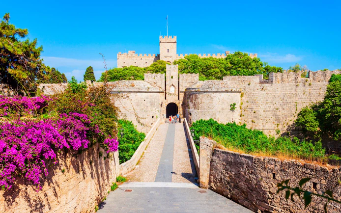 Palace of the Grand Master entrance with stone walls and vibrant flowers, Rhodes, Greece.