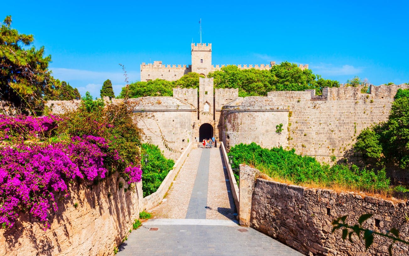 Palace of the Grand Master entrance with stone walls and vibrant flowers, Rhodes, Greece.