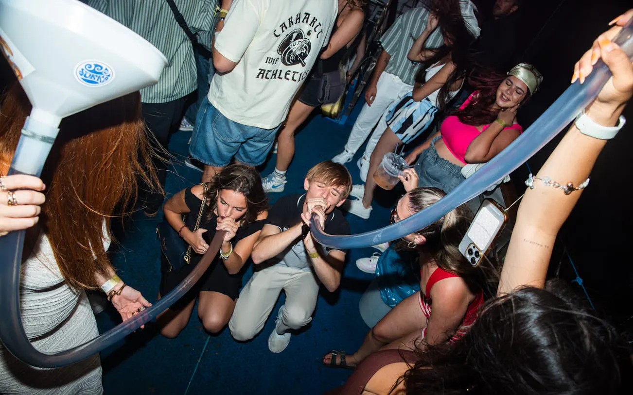 Partygoers enjoying a beer bong on a Split night boat party with a live DJ and free shots.