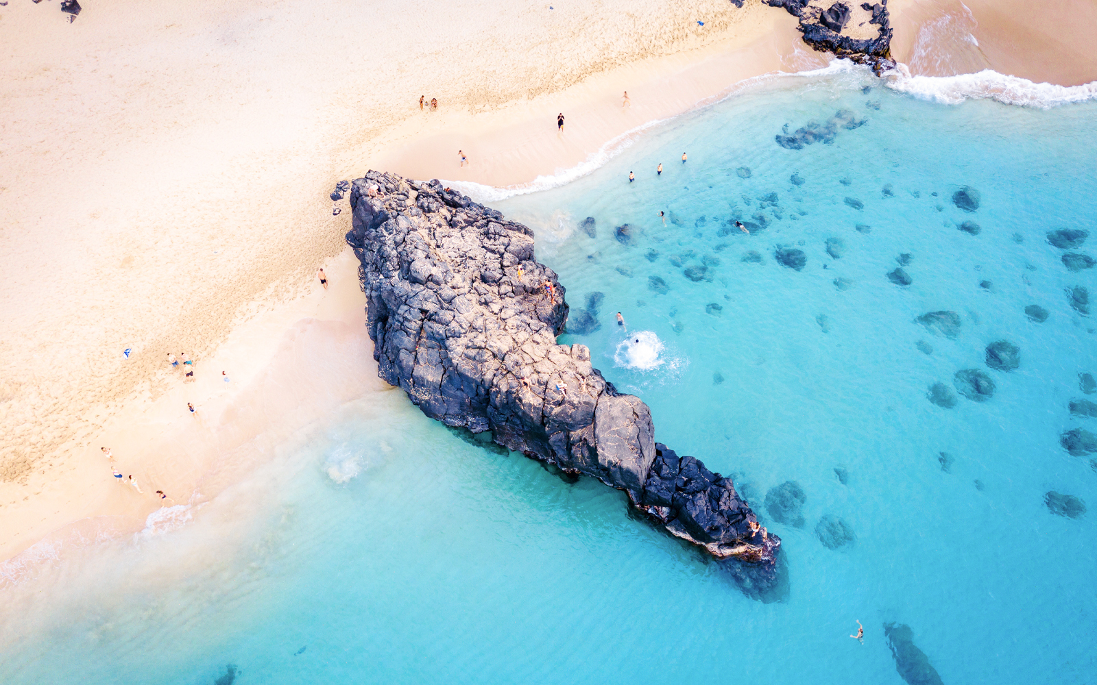 Waimea Beach rock formation with swimmers in clear blue water, Oahu, Hawaii.