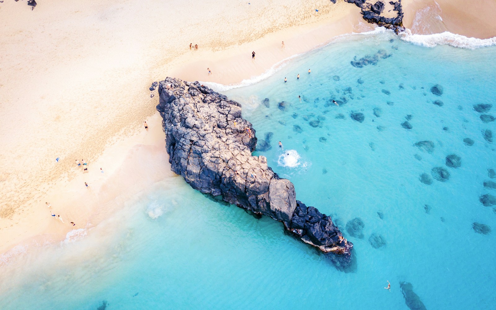 Waimea Beach rock formation with swimmers in clear blue water, Oahu, Hawaii.