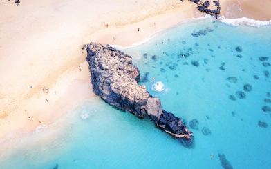Waimea Beach rock formation with swimmers in clear blue water, Oahu, Hawaii.