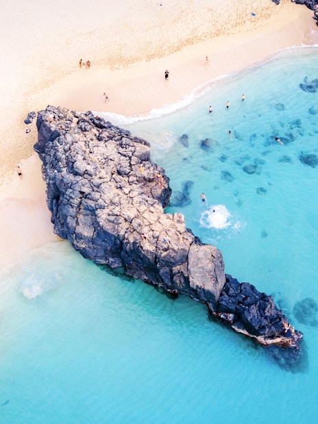 Waimea Beach rock formation with swimmers in clear blue water, Oahu, Hawaii.