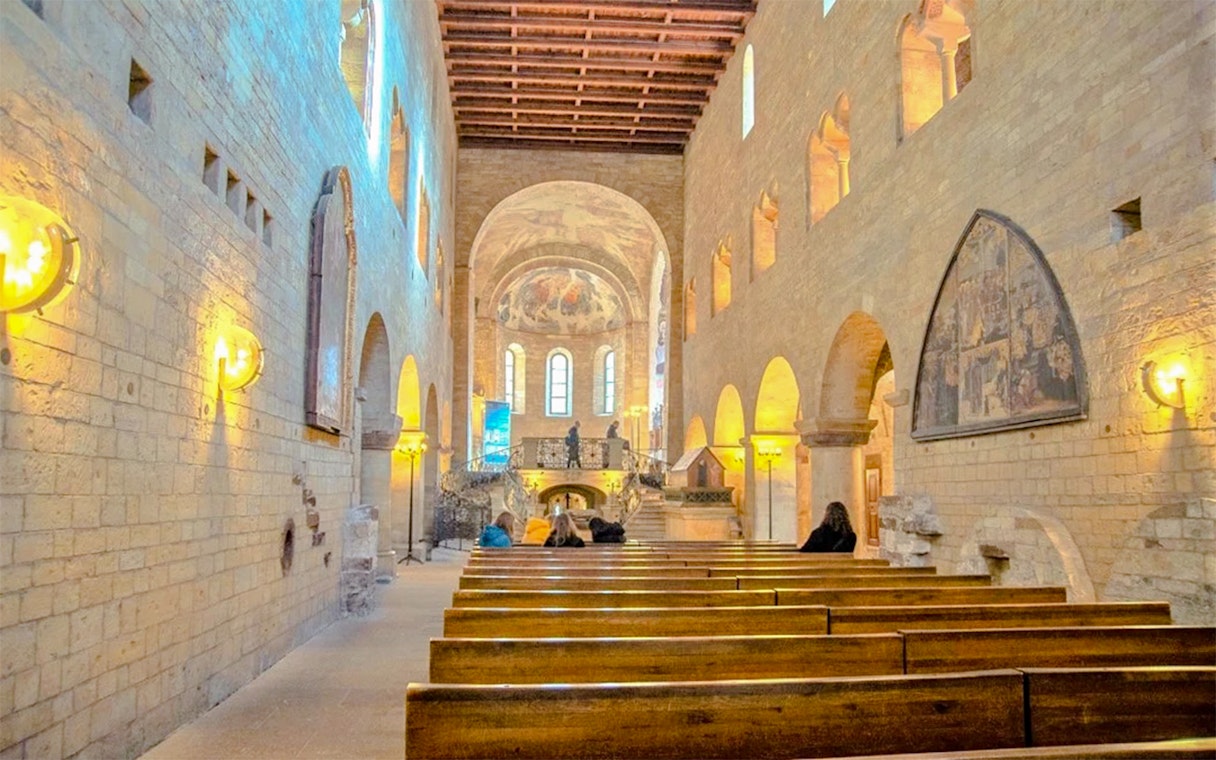 Interior of Basilic of St George with wooden pews and arched windows.