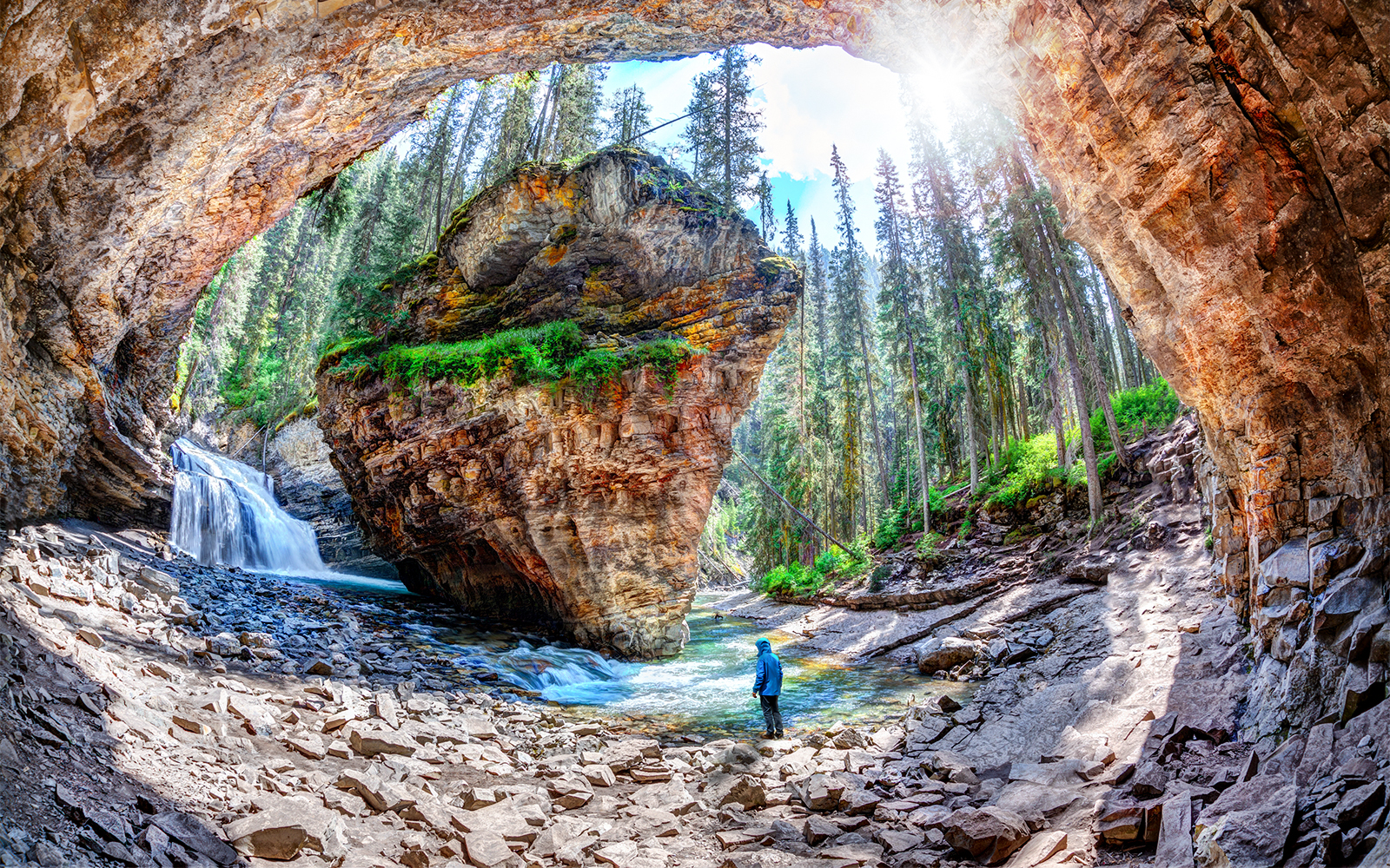 Hiker exploring Johnston Canyon Cave with waterfall in Banff National Park, Canada.