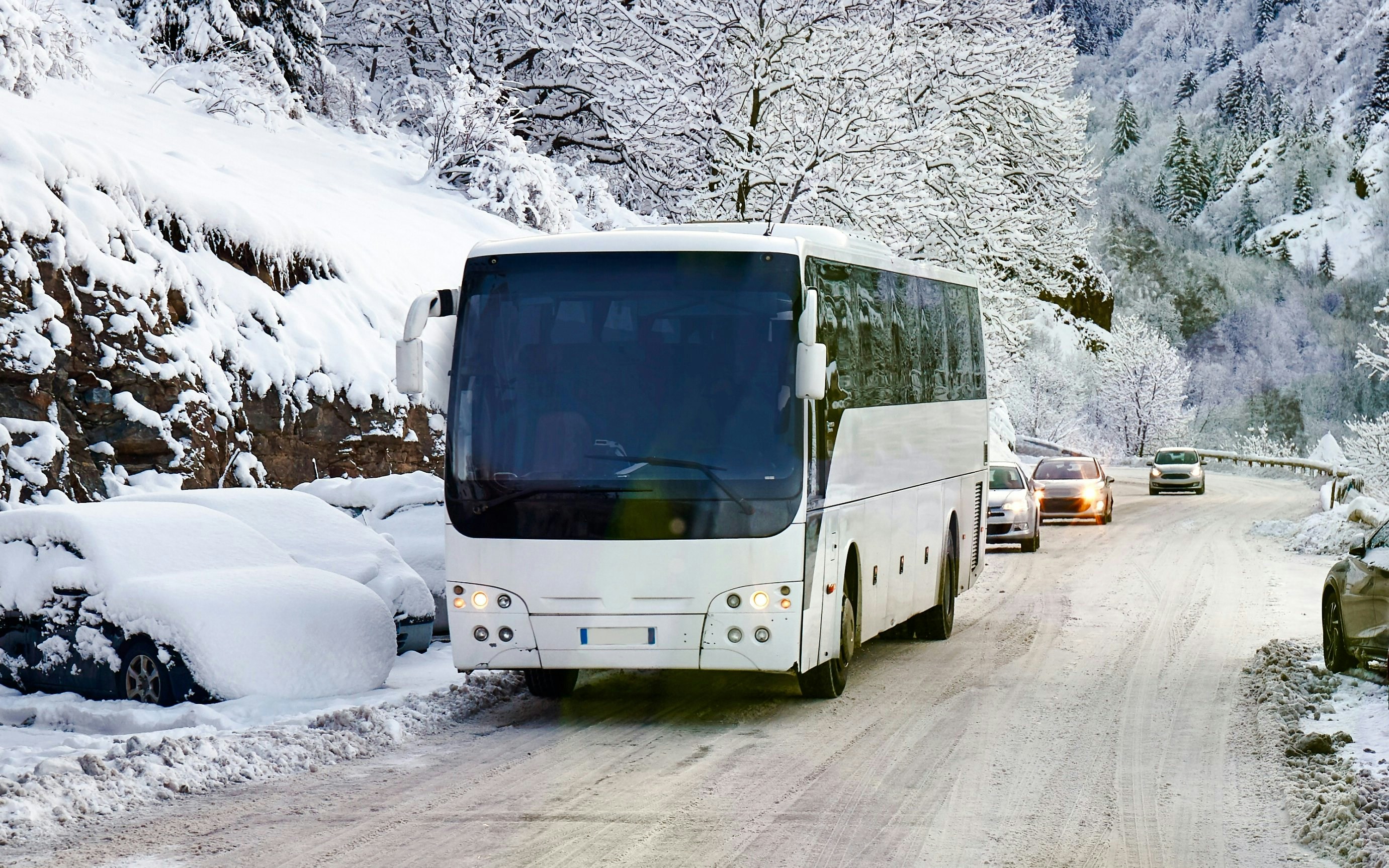 Bus traveling on snowy mountain road with cars following.