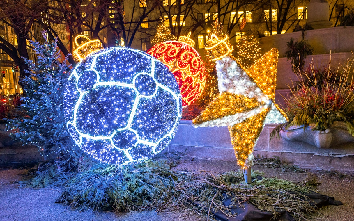 Holiday lights display with illuminated ornaments and star in a city park.