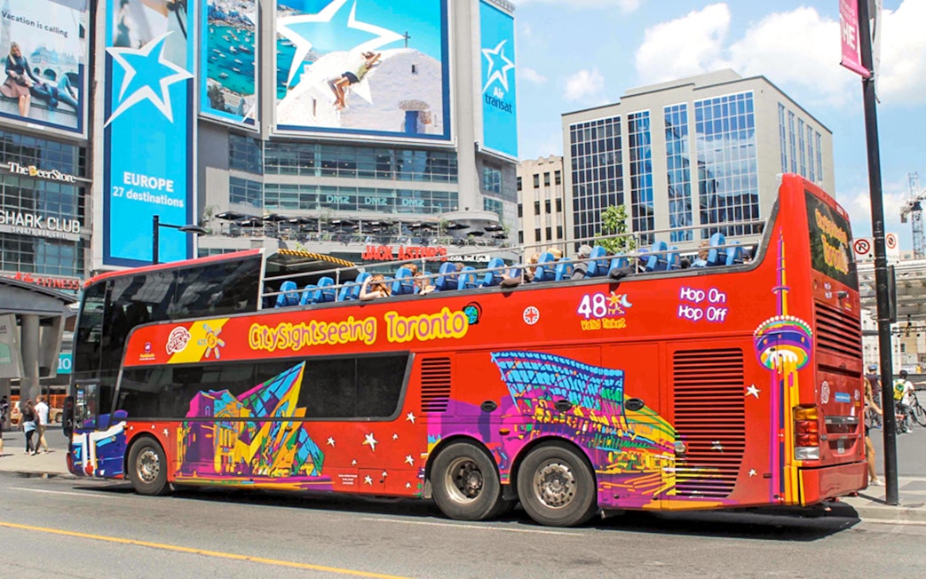 Open top Toronto Hop-On Hop-Off bus near city billboards.